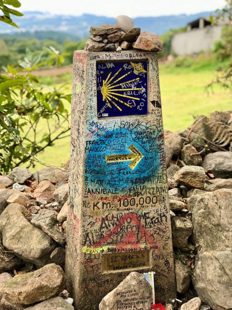 Stone Camino de Santiago waymarker standing beside the trail in Galicia, counting down the kilometres