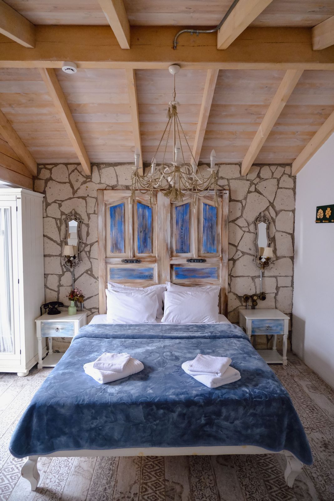 Cozy guesthouse bedroom with wooden beamed ceiling, stone wall and soft blue and white bedding