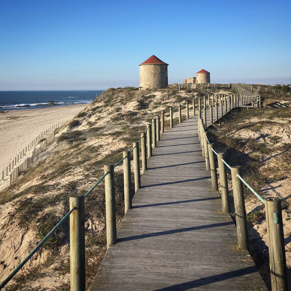 Wooden boardwalk running past sandy dunes and historic windmills along Apulia beach in northern Portugal