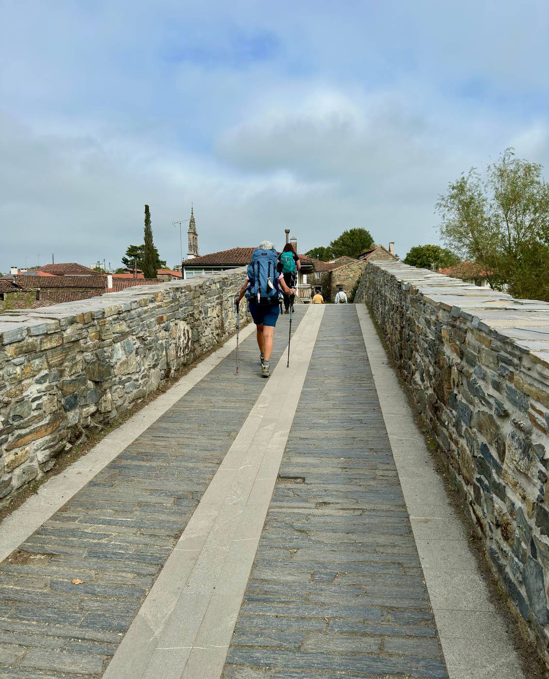Two pilgrims with backpacks seen from behind walking a historic stone path on the Camino de Santiago