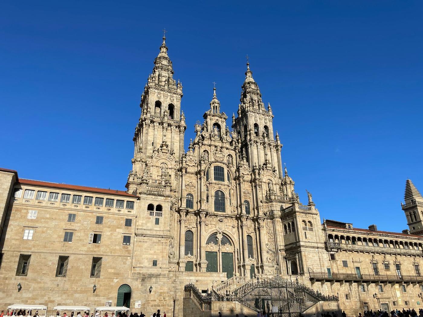 The baroque west facade of Santiago de Compostela cathedral rises against a clear blue sky